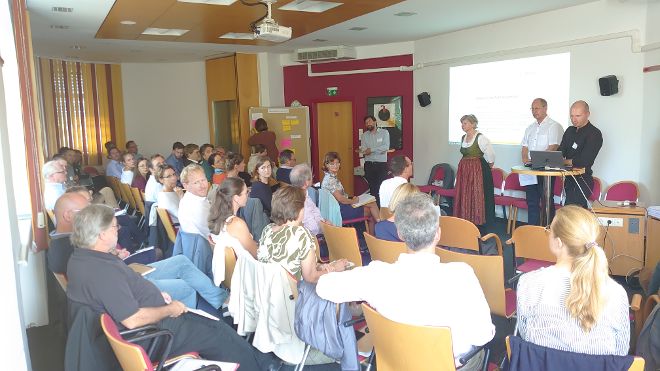 Die Teilnehmenden der Veranstaltung stellen Fragen an die Vortragenden Elsa Brunner, Christian Rosenwirth und Elias Molitschnig. Eine Person notiert im Hintergrund an der Pinwand das Gesagte.