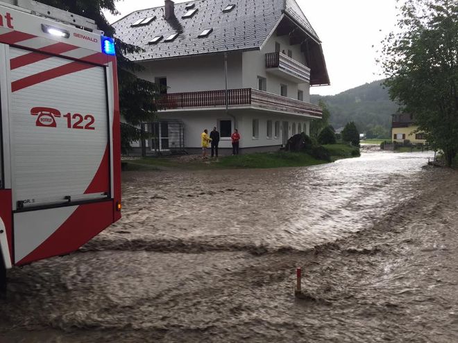 Überschwemmung vor einem Haus mit Feuerwehrauto.