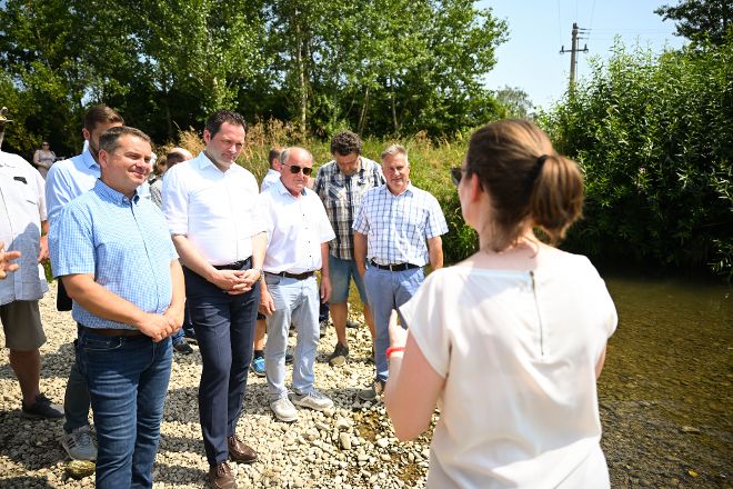 Menschen stehen an einem Kremsufer und hören den Ausführungen einer Mitarbeiterin der Wasserwirtschaft des Landes Oberösterreich zu