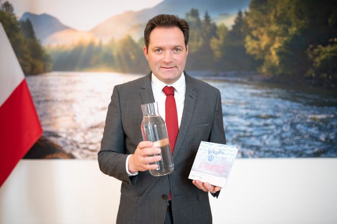 Bundesminister Totschnig hält einen Wasserkrug und den Trinkpass 2023