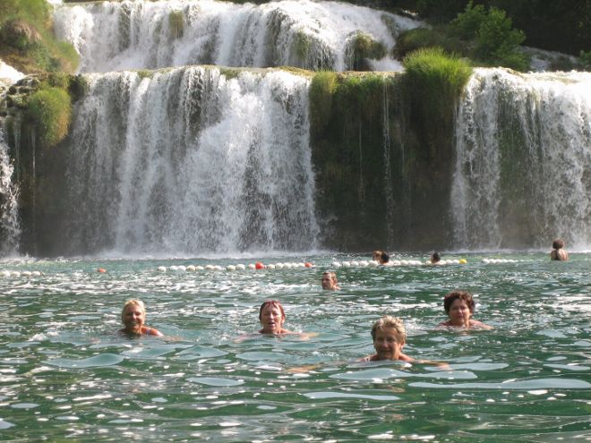 Am Foto sind 9 schwimmende Personen vor einem kleinen Wasserfall zu sehen